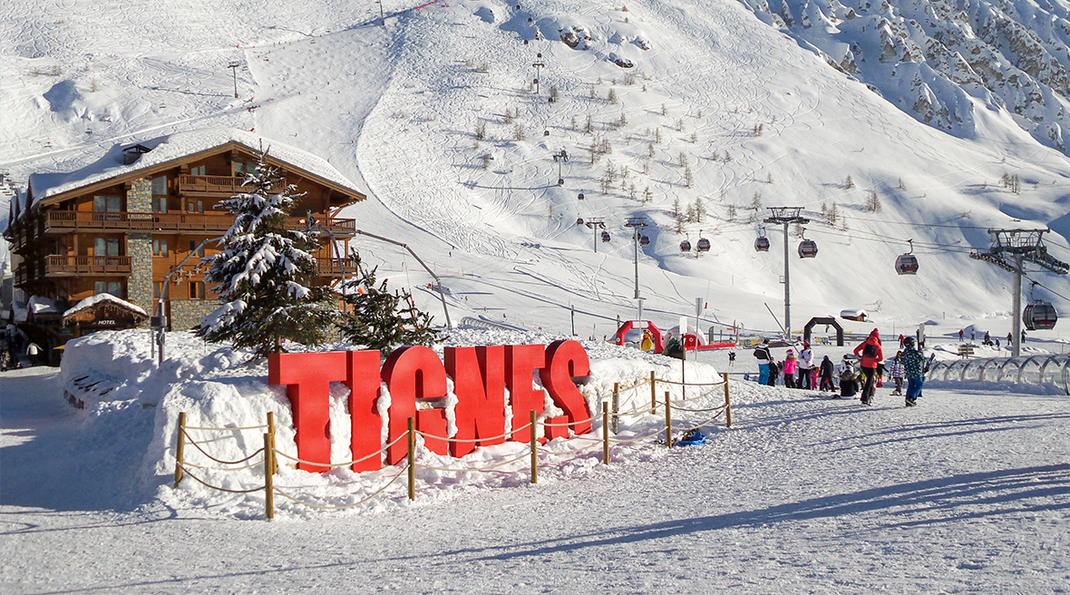 Red letters spelling Tignes in the snow outside ski centre with mountains in background